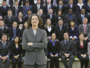 Business Woman Standing In Front Of Business People Sitting In Bleachers, Portrait